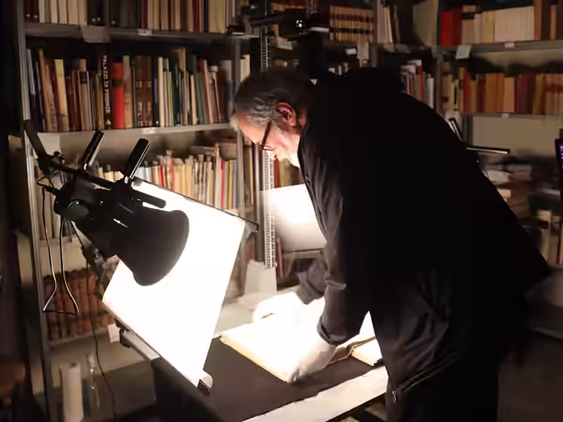 Operatore esperto al lavoro sulla digitalizzazione archivi storici con scanner e luci.