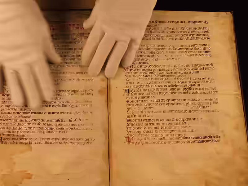 Un operatore con guanti bianchi maneggia una pergamena per la digitalizzazione archivi storici.